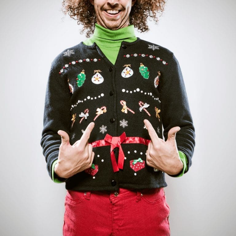 En la imagen se observa un homre sonriendo con un suéter navideño