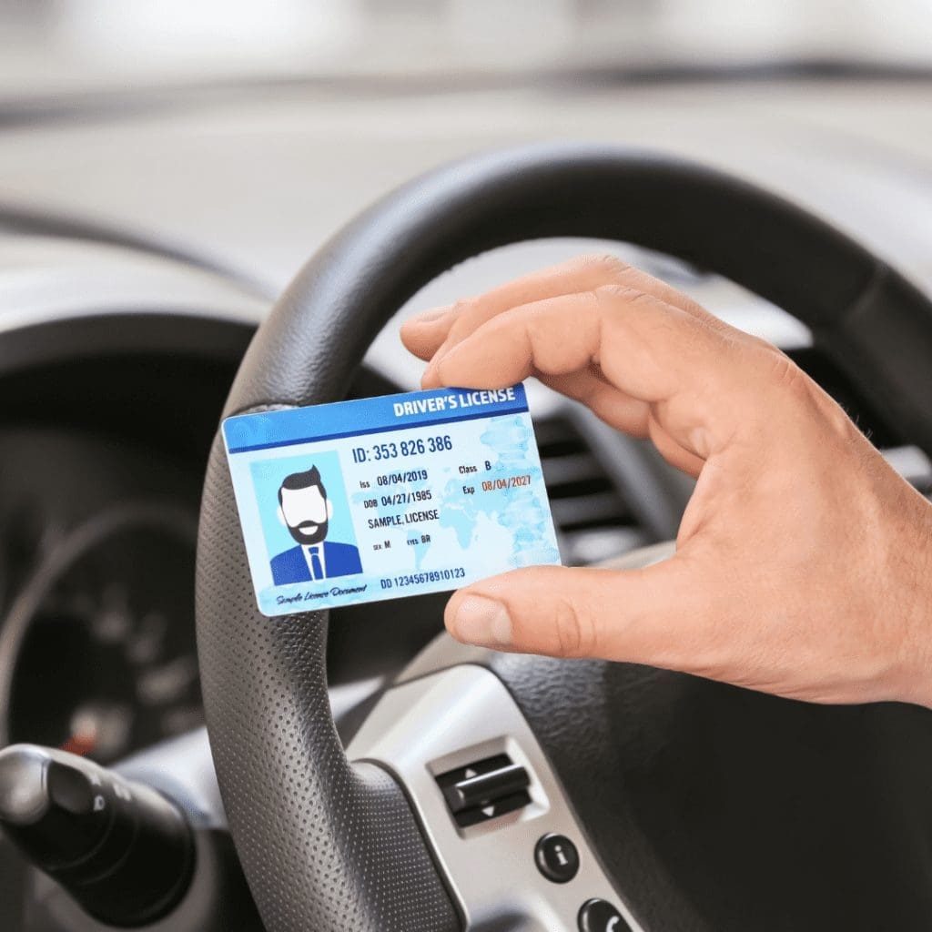 En la imagen se muestra una mano sosteniendo una licencia de conducir, frente a un volante de auto